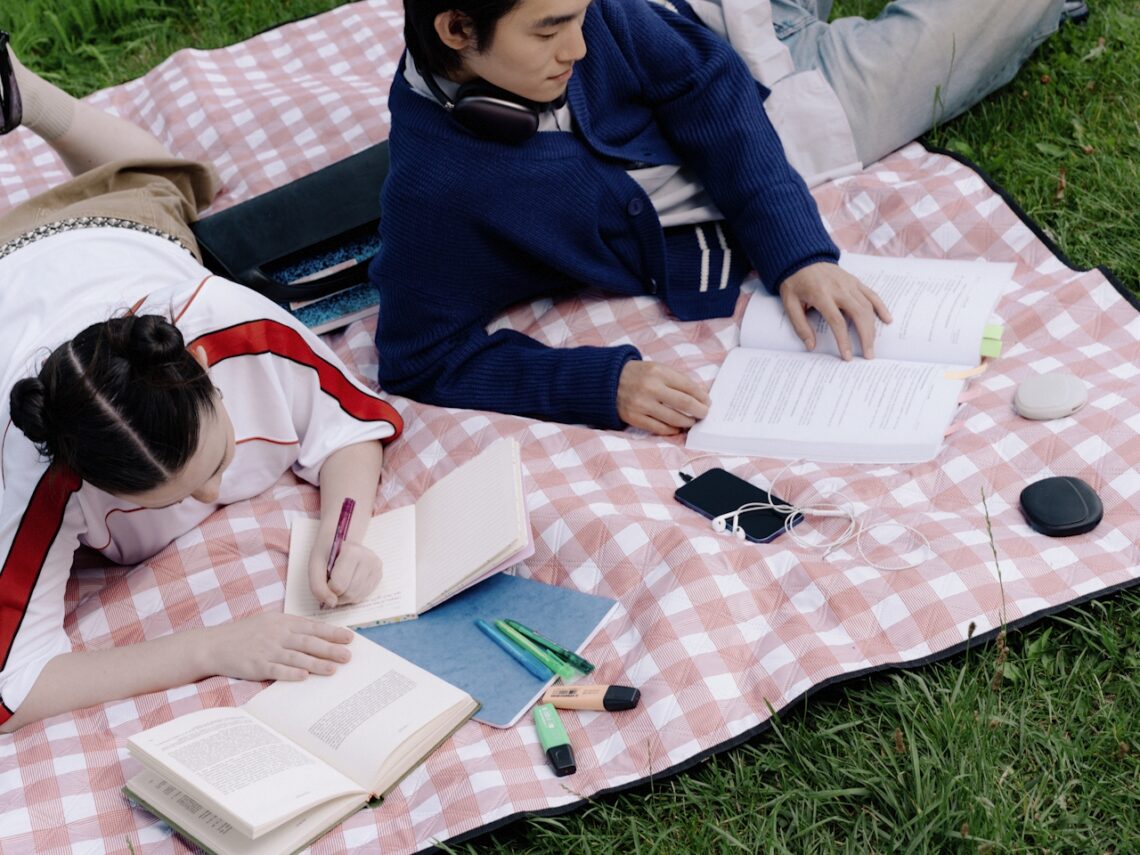 image of two people laying on a blanket int he grass reading