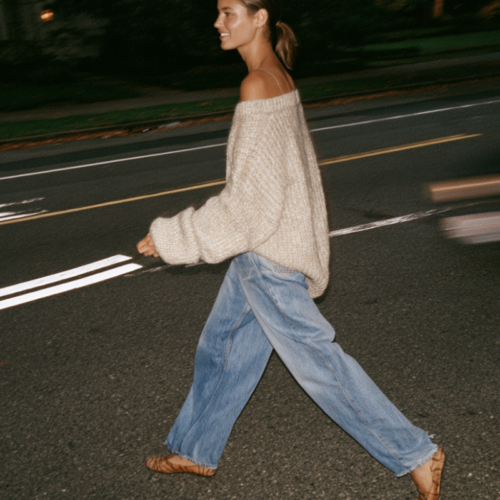 woman walking across street in cozy fall out fit - oversized sweater, baggy jeans and flats